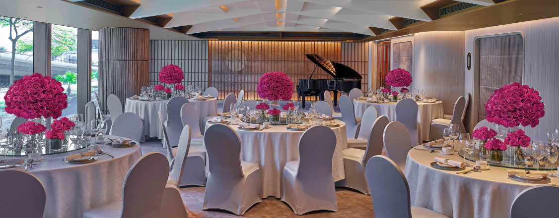 interior of a large ballroom filled with large circular table with white table cloths and pink flower center pieces at a New World Millennium Hong Kong Hotel wedding venue